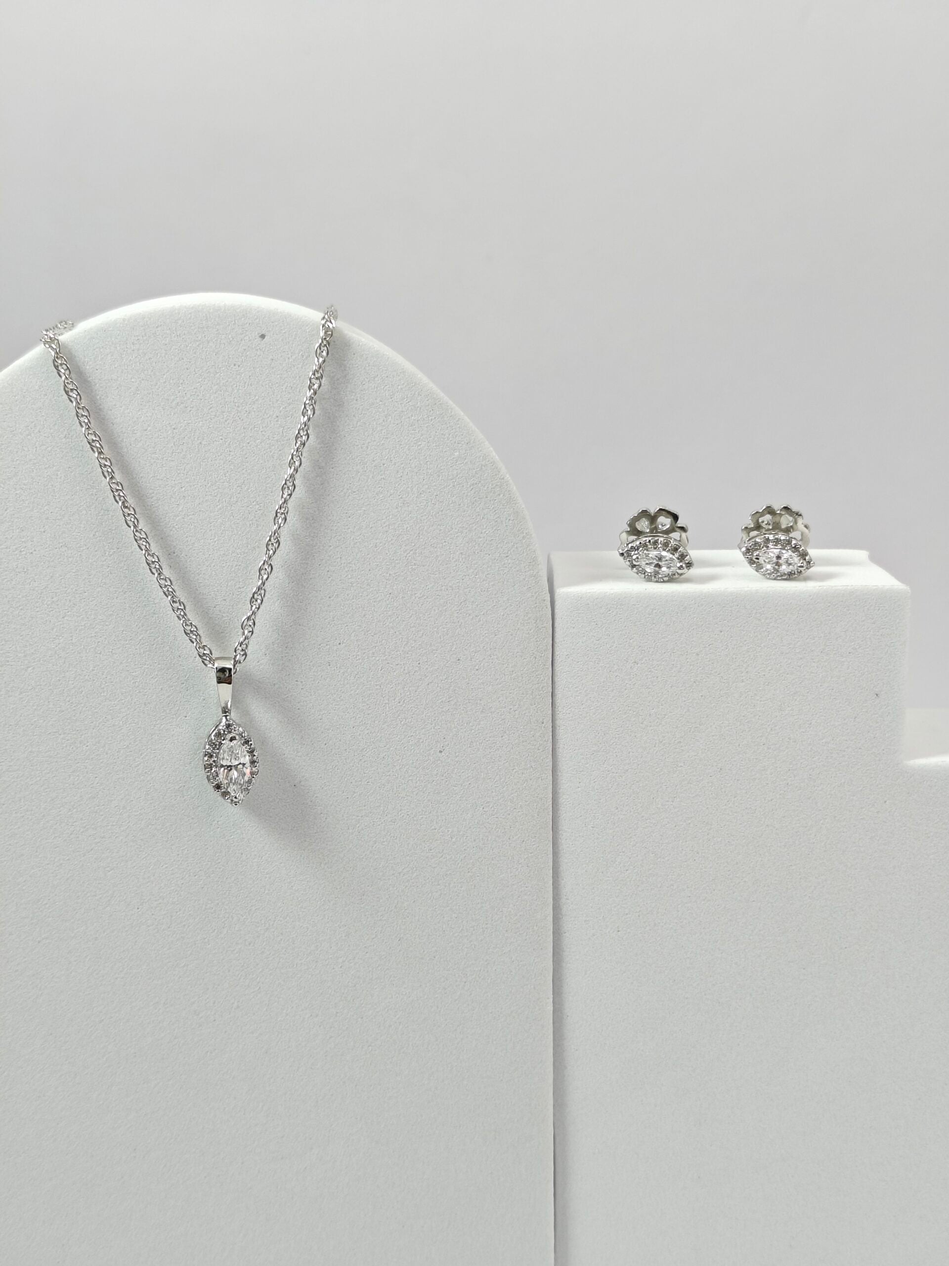 Silver necklace and earrings on a white stand with a light gray background